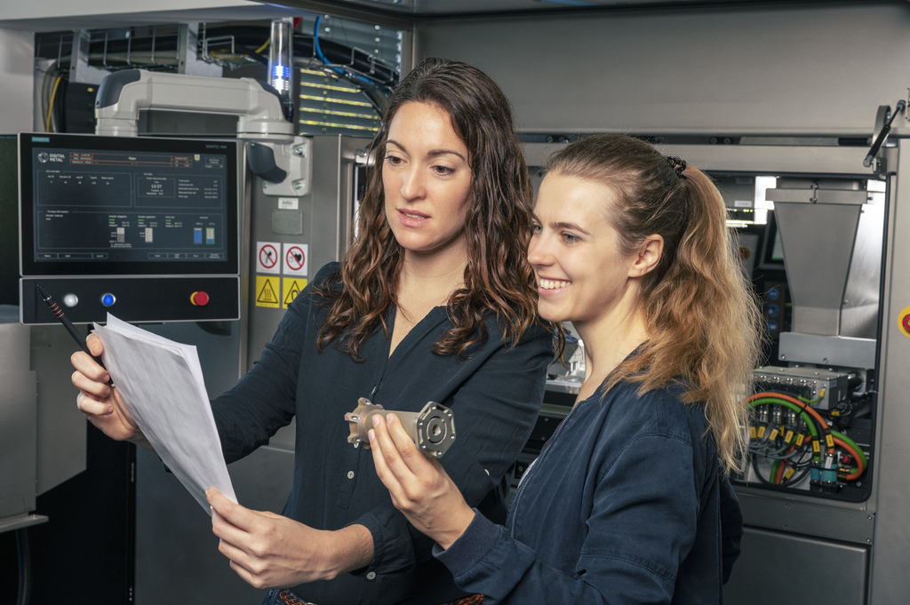 Sara Claramunt und Laura Trinkies schauen auf ein Blatt, im Hintergrund sind Maschinen